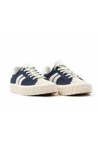 Marinblå och krämfärgade mockasneakers med en texturerad beige gummisula och triangulärt mönster på yttersulan, med vita ränder och snörningar.