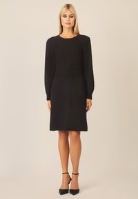Sort strikdress med lange ærmer og et struktureret kabelmønster på overdelen, A-linjeformet og knælængde. Moderne, minimalistic design.