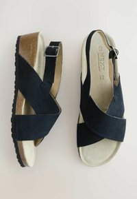 Sandales en daim noir avec des brides croisées, une boucle ajustable et une semelle en liège légère. Doublure intérieure douce pour un confort optimal.