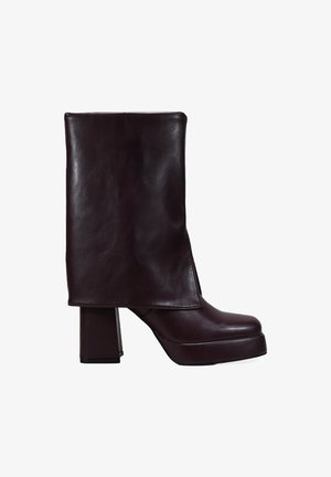 Bottine en cuir bordeaux avec un talon épais et une tige haute et structurée. Texture lisse avec un design élégant et un minimalisme dans les détails.