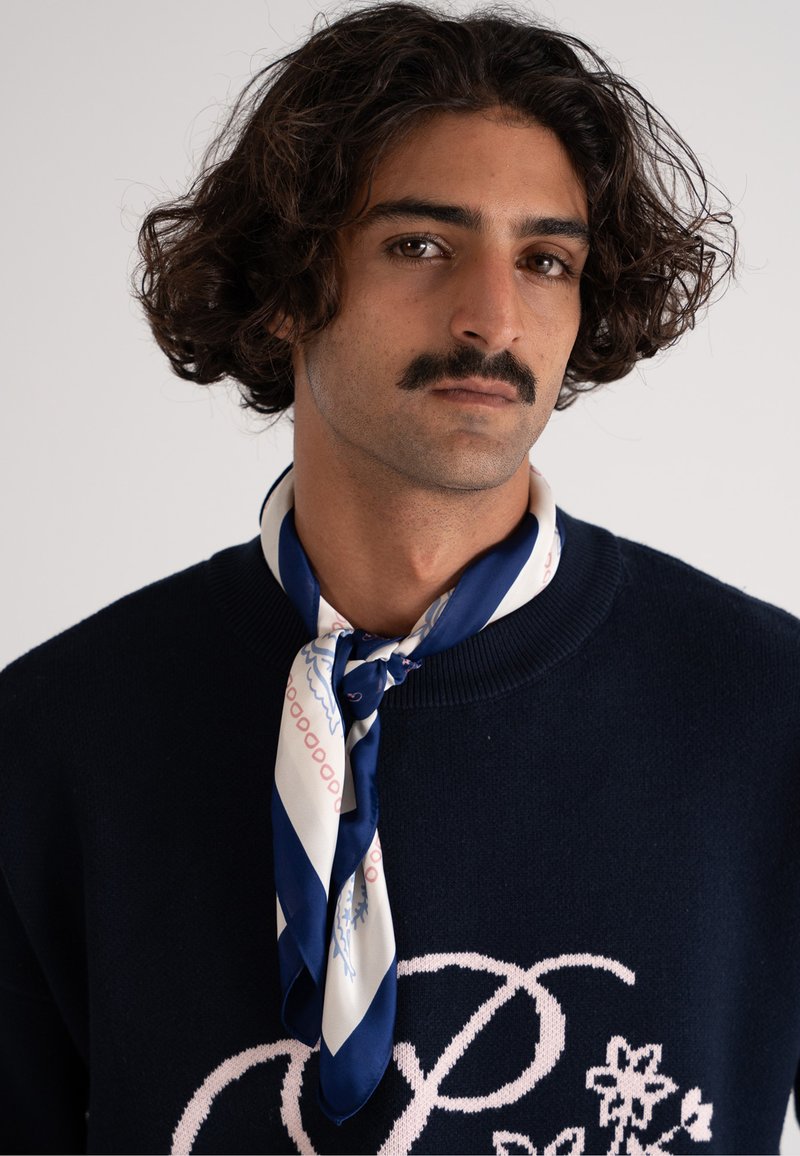 Maglione blu con design floreale rosa e testo, abbinato a una sciarpa di seta con strisce diagonali e motivi blu, bianchi e rosa.
