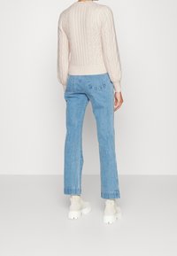 Jasnoróżowy sweter w splot warkoczowy, niebieskie dżinsy o prostym kroju oraz kremowe buty na grubej podeszwie, prezentujące teksturowany design i luźny fason.