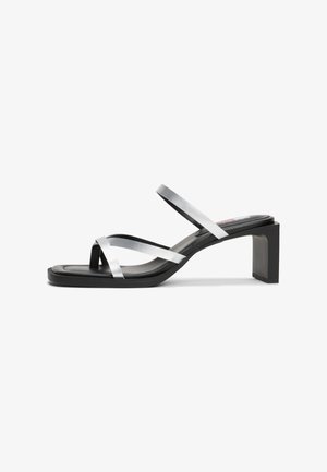 Sort hæl sandal med to metaliske sølvstropper og firkantet tå. Har en kraftig blokhæl og en glat, mat finish.