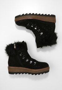 Botas de tobillo forradas de piel negra con adornos de joyas y suelas en zigzag, vistas desde arriba y ligeramente de lado.