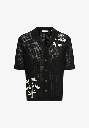 Musta lyhythihainen neulepaita, jossa napitettava edusta ja avoin kudoskuvio. Rintakehässä ja alalaidassa valkoiset kukkaompeleet.