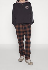 Sudadera negra con capucha gris y logo, combinada con pantalones de cuadros en tonos marrón y negro, y zapatillas gris claro.