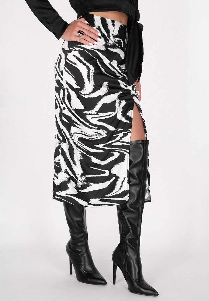 Fustă midi cu dungi de zebră alb-negru, cu fante pe lateral, realizată dintr-un material neted, asortată cu cizme negre cu toc stiletto înalt pentru un look elegant.