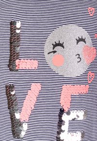 Jiskřivé písmena tvořící slovo "LÁSKA" na modro-bílém pruhovaném látce, s lesklou tváří, která mrká a posílá polibek ve tvaru srdce.