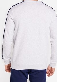 Sudadera gris con cuello redondo, rayas en los hombros de color azul marino, puños y dobladillo acanalados. Material suave y texturizado de mezcla de algodón.