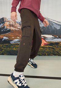 Bruine cargo sweatpants met verstelbare tailleband en elastische boorden, voorzien van twee grote zijzakken en een subtiele slijtage-detail.