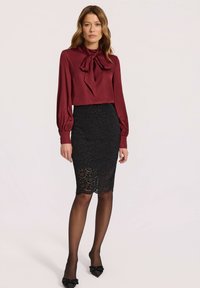 Bordeaux bluzka z kokardą, długie rękawy; czarna koronkowa spódnica ołówkowa z falbaniastym wykończeniem; czarne rajstopy i czółenka na szpilce. Prosty i elegancki design.