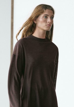 Brun langærmet sweater med høj hals. Blød tekstur og afslappet pasform med sænkede skuldre og minimalistisk design.