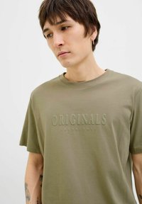 Bardžios žalios medvilnės marškiniai su subtiliu įspaudu „ORIGINALS JACK & JONES“ priekyje. Apvalus kaklas, trumpomis rankovėmis, laisvas kirpimas.