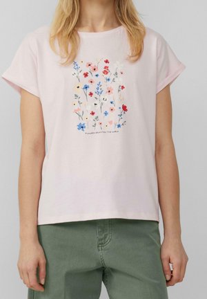 Personne portant un t-shirt rose clair avec un motif floral coloré et le texte "Flowers brighten the world" au centre.