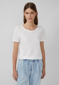 Weißes kurzärmliges T-Shirt mit rundem Ausschnitt und umgeschlagenen Ärmeln, aus leichtem Stoff, kombiniert mit hellblauen, lässig sitzenden Jeans.