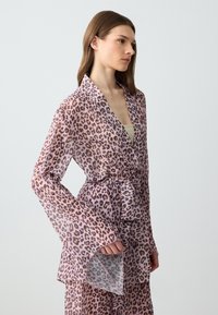 Robe leopardato trasparente di un leggero rosa con maniche lunghe a campana, cintura da annodare in vita e colletto; il tessuto ha una trama delicata.