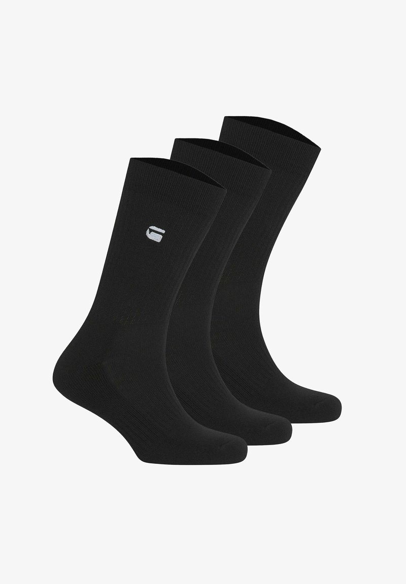 Trois chaussettes noires de type sportif avec un petit logo blanc sur le côté, présentées debout et alignées en rangée.