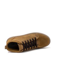 Zapatilla de ante marrón con cordones marrón oscuro, puntera redondeada y detalles de costura sutiles; presenta una suela de goma texturizada y un tirador.