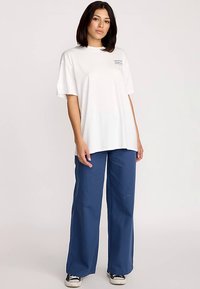 Wit katoenen T-shirt met korte mouwen, gecombineerd met blauwe broek met wijde pijpen. Casual stijl, met een eenvoudig ontwerp zonder patronen of accenten.