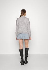 Maglione grigio a maglia, gonna in denim blu chiaro con pieghe e stivali neri alti fino al ginocchio; minima texture con una silhouette rilassata e design semplice.