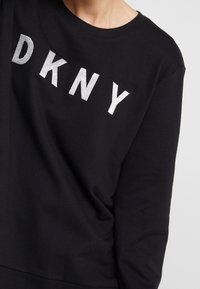 Person wearing a black sweatshirt with large white embroidered letters "DKNY" across the chest.