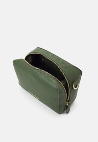 Zelená texturovaná kožená crossbody taška se zlatým zipem částečně otevřená, ukazující vnitřní kapsu a zlatý kovový kroužek na straně.