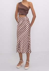 Ruskea satiininen olkapään paljastava lyhyt yläosa yhdistettynä ruskeavalkoiseen ruutukuosiseen midi-hameeseen. Malli käyttää korokepohjaisia sandaaleja.