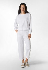 Sudadera blanca de algodón con mangas largas y corte rectángulo, combinada con pantalones de chándal blancos de algodón que cuentan con bolsillos laterales y una silueta relajada.