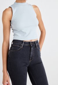 Top corto de canalé color azul claro con cuello alto, combinado con vaqueros de tiro alto color azul oscuro que presentan costuras en contraste y bolsillos frontales.
