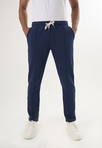 Marina joggers med dragsko i midjan, sidofickor och en figurnära passform. Tillverkade av mjukt tyg, med vita detaljer och dragkedjor vid vristerna.