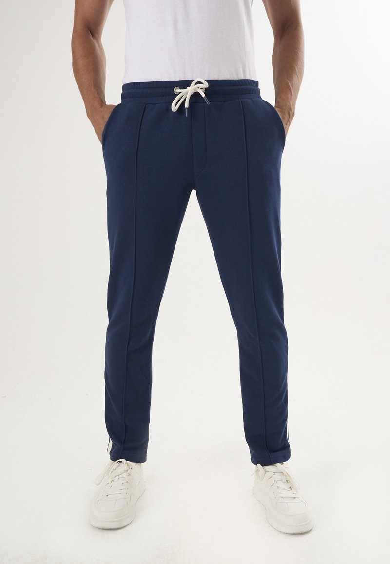 Marina joggers med dragsko i midjan, sidofickor och en figurnära passform. Tillverkade av mjukt tyg, med vita detaljer och dragkedjor vid vristerna.