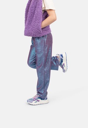 Pantalons de sport en métal violet brillant avec une coupe décontractée, associés à des chaussures de course violettes et bleues claires. Gilet doux et texturé de couleur violette.