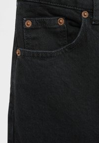 Jean en denim noir avec une poche avant ornée de rivets en cuivre, des coutures visibles et une texture lisse, mettant en avant la durabilité du tissu.