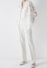 White lace button-up shirt with floral patterns, paired with tailored white trousers and glossy pointed-toe heels with metallic accents.