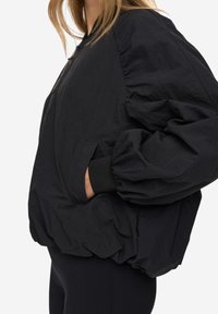 Černá bombera z lehké látky s volnějším střihem, nafouklými rukávy, elastickými manžetami a bočními kapsami.