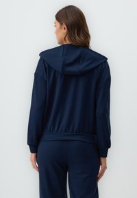 Navy hoodie with a relaxed fit, drawstring hood, and long sleeves. The fabric appears smooth and stretchy, with a gathered waistband.