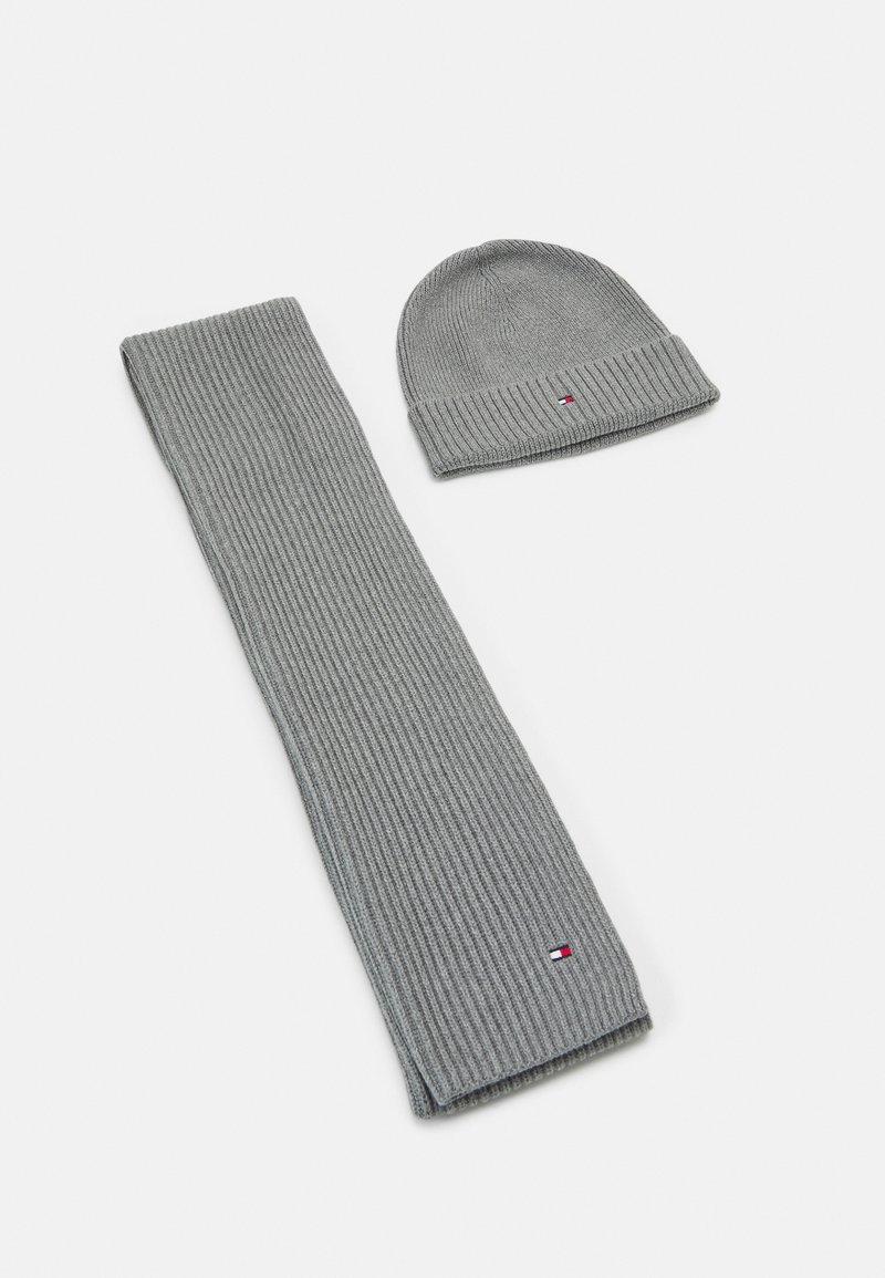 Écharpe en maille côtelée grise et bonnet assorti avec petit logo rectangulaire rouge, blanc et bleu sur fond blanc.