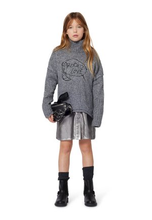 Pull en maille gris à col roulé avec un motif "RODEO LOVE", associé à une jupe argentée brillante, des bottines noires à la cheville et un petit sac noir.