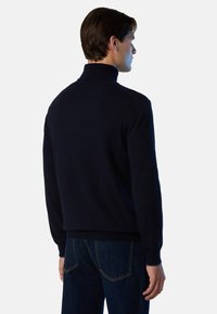 Maglione in maglia blu navy con collo alto e polsini a coste, realizzato in tessuto morbido, indossato con jeans scuri in denim.