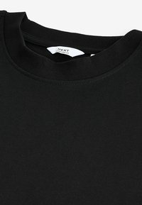 Zwarte gekatoene oversized t-shirt met een geribbeld textuur en ronde halslijn, met een label genaaid aan de kraag.