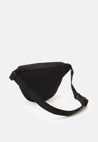 Juodas fanny pack'as, pagamintas iš patvarios medžiagos, turintis kreivių dizainą, reguliuojamą diržą ir užtrauktuku užsegamą skyrių priekyje.