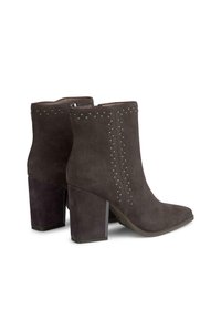 Botas de tobillo de ante en gris oscuro con tacones cuadrados gruesos, que cuentan con adornos de tachuelas en la parte frontal para un detalle adicional.
