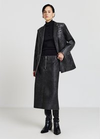 Blazer in pelle nera con cuciture bianche a contrasto, abbinato a un dolcevita nero aderente, gonna di jeans a vita alta e stivaletti.