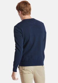 Námořnicky modrý pletený svetr s kulatým výstřihem, dlouhými rukávy a žebrovanými manžetami a lemem. Tkanina působí hladce a lehce.