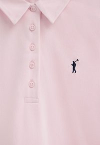 Lichtroze poloshirt met vier knopen en een kleine marineblauwe geborduurde figuur die een golfclub vasthoudt op de borst.