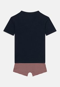 Μπλε ναυτικό κοντομάνικο πουκάμισο σε συνδυασμό με σορτς με κόκκινο και λευκό μοτίβο, τοποθετημένα πάνω σε λευκό φόντο.