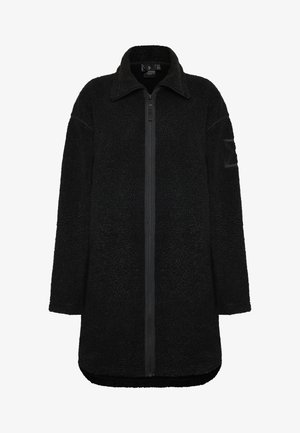 Mustas fleece-takki, jossa on vetoketju edessä, suuri kaulus, pitkät hihat ja teksturoitu pinta. Vasemmassa hihassa on paikka.