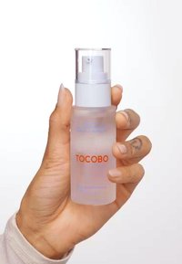 Bouteille pulvérisateur transparente avec un capuchon à pompe blanche, portant 'TOCOBO' en lettres orange en gras. Surface lisse, forme cylindrique, design minimaliste.