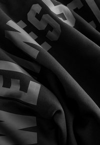 Black fabric showing a smooth texture, with large gray graphic lettering partially visible, creating a layered look.