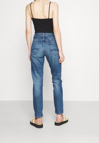 Jeans de mezclilla azul de tiro alto con corte recto, que cuentan con dos bolsillos traseros con costuras onduladas y una textura desvanecida, combinados con una blusa negra.